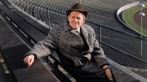 Sepp Herberger posiert in einem leeren Stadion mit Hut für ein Foto.