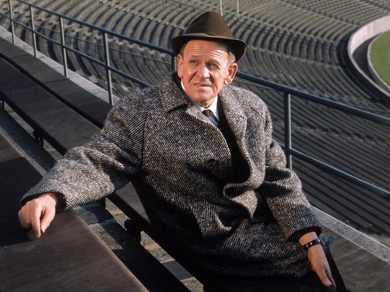 Sepp Herberger posiert in einem leeren Stadion mit Hut für ein Foto.