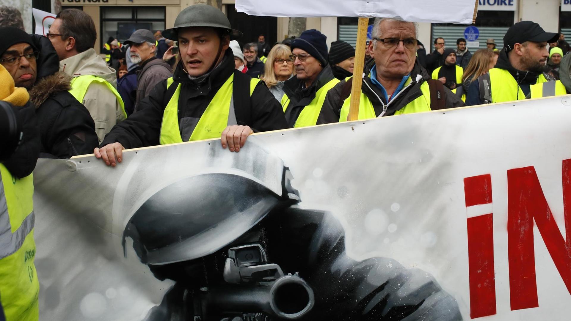Demonstranten halten während des Protests der "Gelbwesten" ein Transparent, das einen Polizisten mit einer Waffe abbildet.