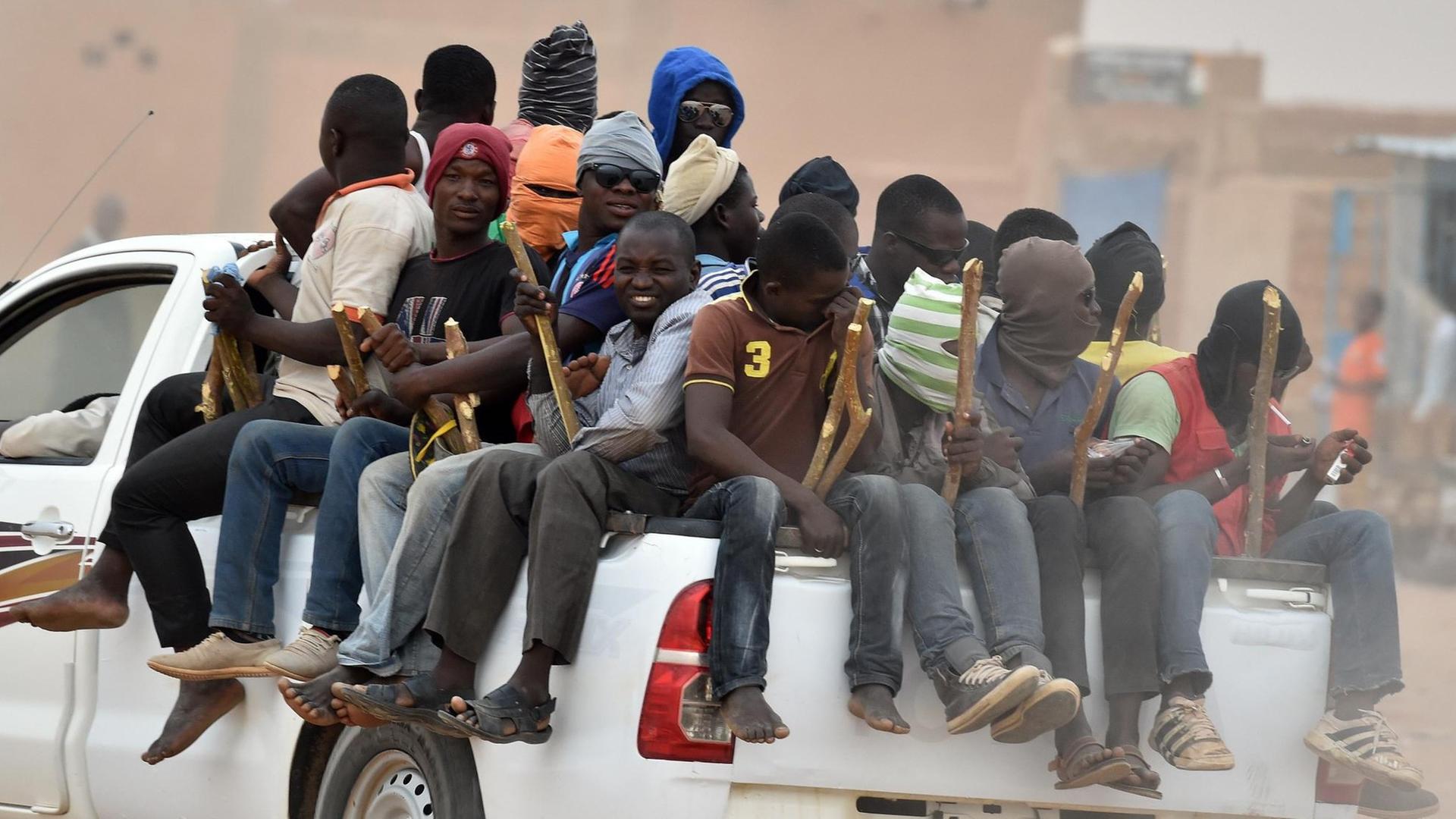 Flüchtlinge sitzen auf der Ladefläche eines Pick-Up-Trucks und halten Holzstöcke, die mit dem Wagen verbunden sind, um nicht herunterzufallen. Flüchtlinge sitzen auf der Ladefläche eines Pick-Up-Trucks und halten Holzstöcke, die mit dem Wagen verbunden sind, um nicht herunterzufallen.