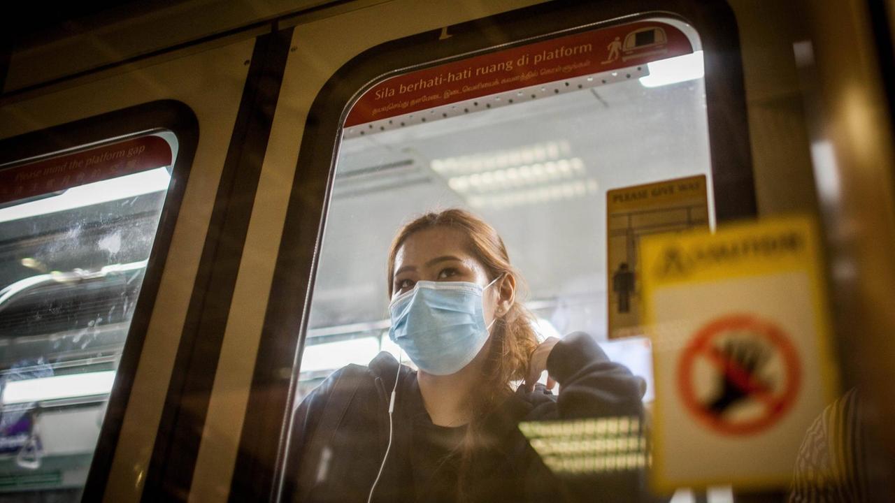 Eine Frau steht im Innern eines U-Bahnwaggons und blickt aus dem Fenster. Sie trägt eine Schutzmaske. Eine Frau steht im Innern eines U-Bahnwaggons und blickt aus dem Fenster. Sie trägt eine Schutzmaske.