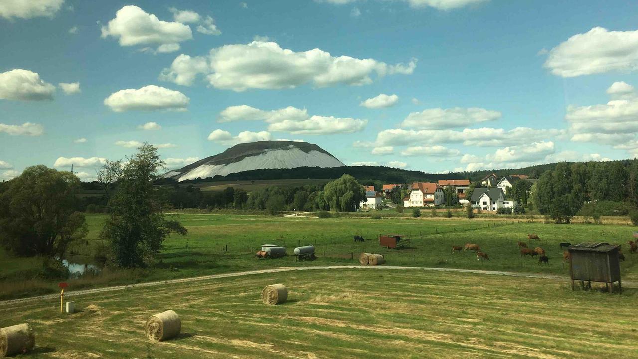 Der Monte Kali aus dem Zug heraus fotografiert. Näher zu den Gleisen Strohrollen und jenseits eines Feldweges weidende Tiere. Der Monte Kali aus dem Zug heraus fotografiert. Näher zu den Gleisen Strohrollen und jenseits eines Feldweges weidende Tiere.