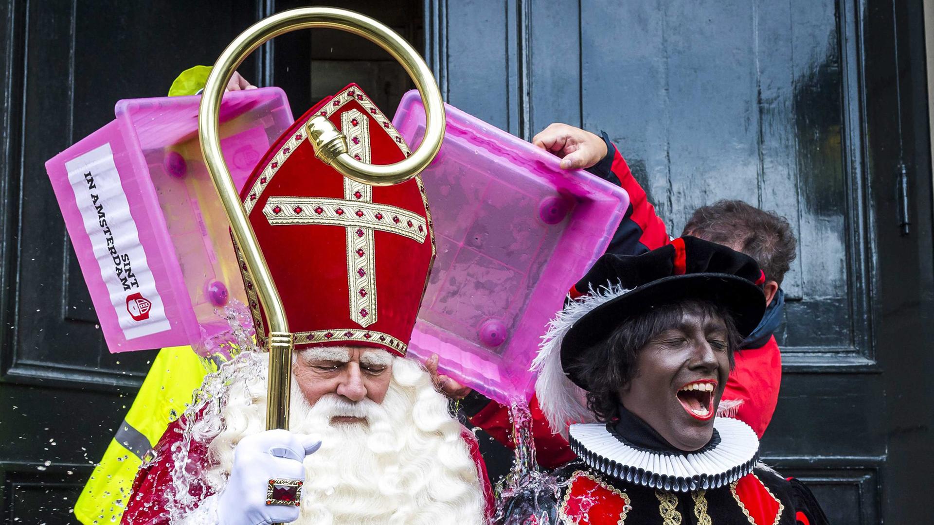 Zwei Darsteller sind verkleidet als Nikolaus mit weißem Bart, roter Bischofsmütze und Mitra und als Zwarter Piet mit schwarz angemaltem Gesicht in einem schwarzem Kostüm mit Karos. Zwei Darsteller sind verkleidet als Nikolaus mit weißem Bart, roter Bischofsmütze und Mitra und als Zwarter Piet mit schwarz angemaltem Gesicht in einem schwarzem Kostüm mit Karos.