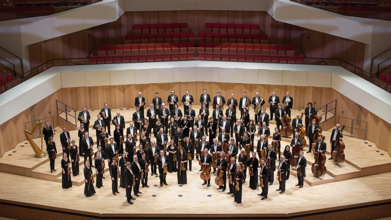 Das Orchester steht in Konzertkleidung auf der Bühne des Dresdner Kulturpalastes. Das Orchester steht in Konzertkleidung auf der Bühne des Dresdner Kulturpalastes.