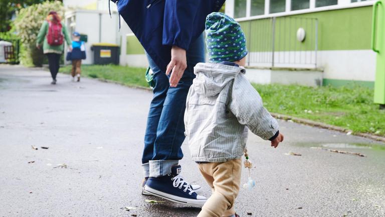 Ein Kind und seine Mutter gehen zum Eingang einer Kita. Heute startet in Berlin wieder der eingeschränkte Regelbetrieb für Kitas.