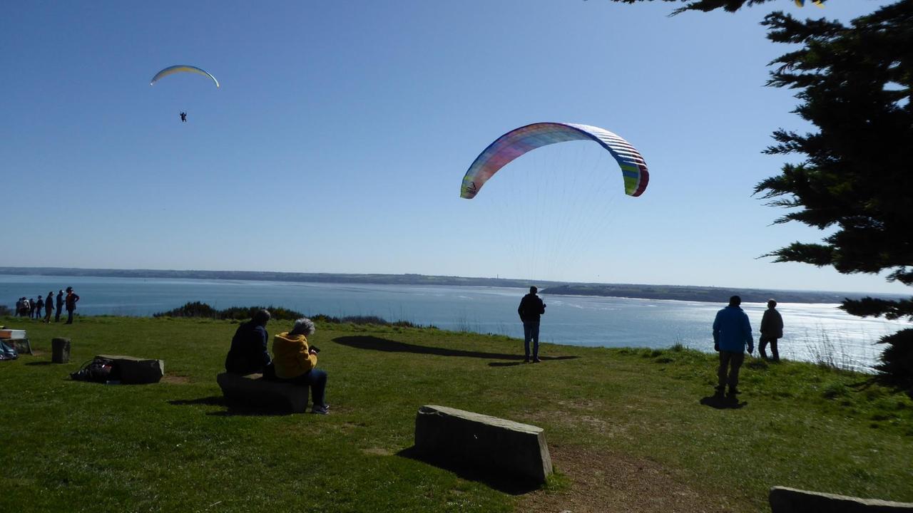 Eine große Wiese vor Küste und Meer mit einigen Menschen und Paraglidern. Eine große Wiese vor Küste und Meer mit einigen Menschen und Paraglidern.