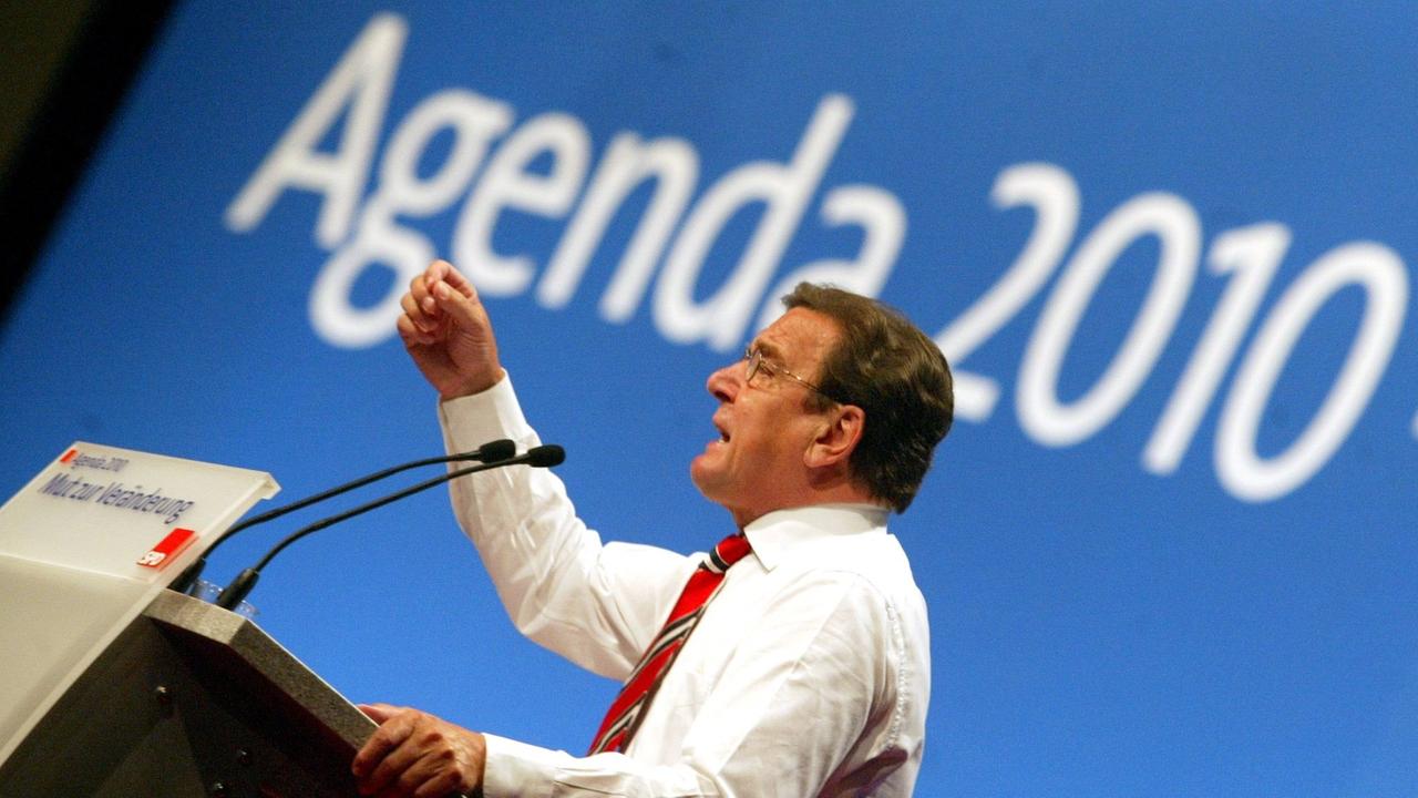 Gerhard Schröder bei einer Rede am Stehpult, hinter ihm an die Wand projiziert steht "Agenda 2010"