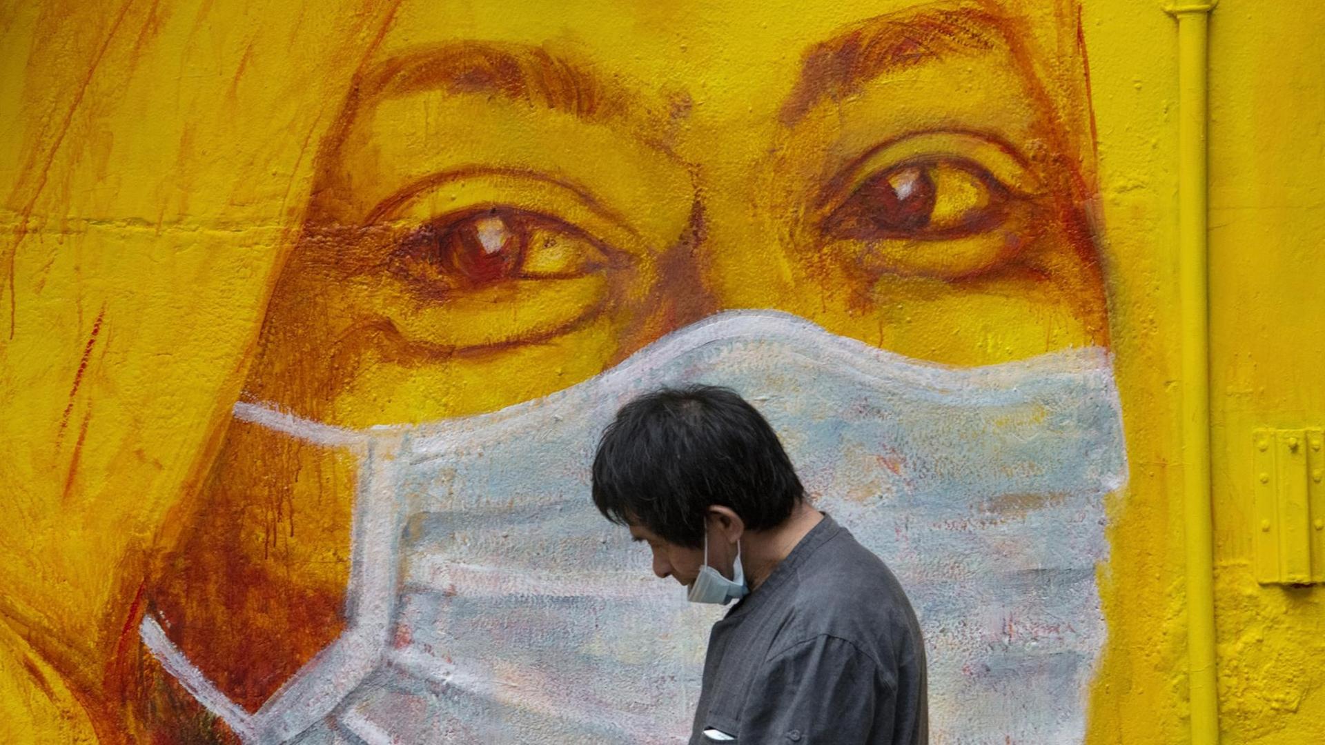 Ein Mann mit Maske geht in Hongkong an einem Graffito mit einer masketragenden Frau vorbei Ein Mann mit Maske geht in Hongkong an einem Graffito mit einer masketragenden Frau vorbei