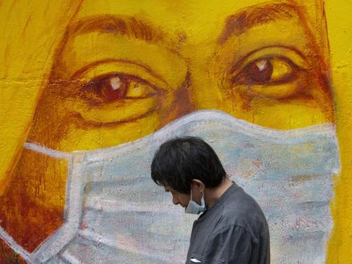 Ein Mann mit Maske geht in Hongkong an einem Graffito mit einer masketragenden Frau vorbei