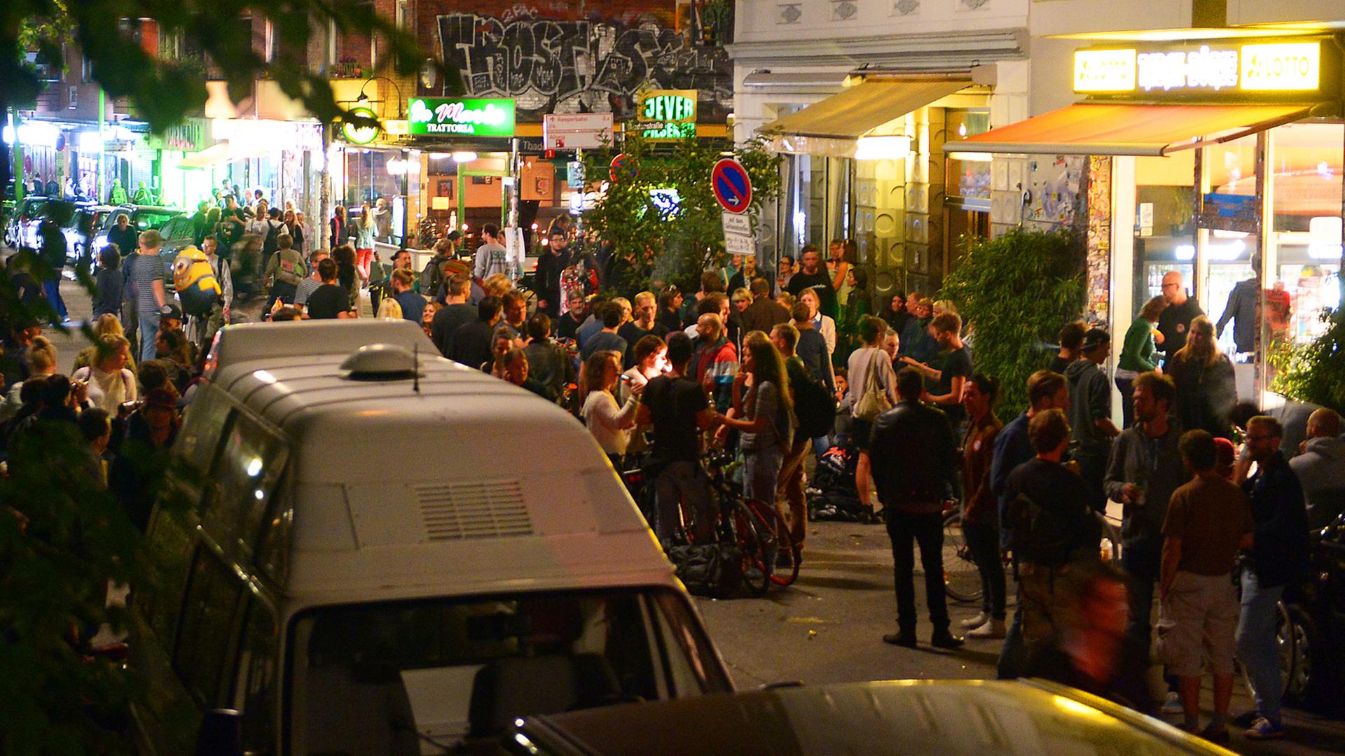 Junge Erwachsene stehen abends in einem Ausgehviertel auf der Straße und trinken. Junge Erwachsene stehen abends in einem Ausgehviertel auf der Straße und trinken.