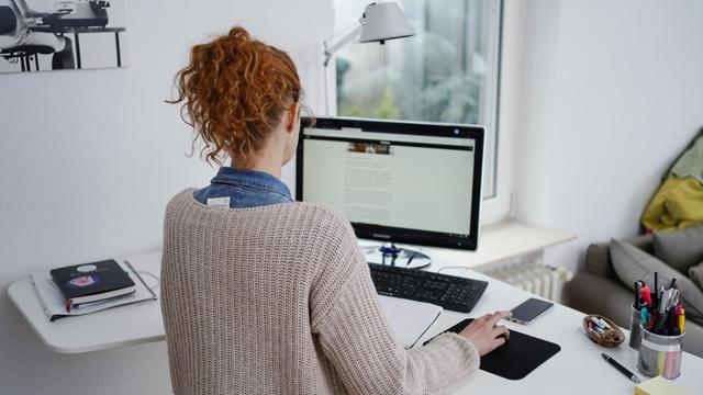 Eine Frau arbeitet in ihrer Wohnung vor einem Computer an einem Stehtisch.