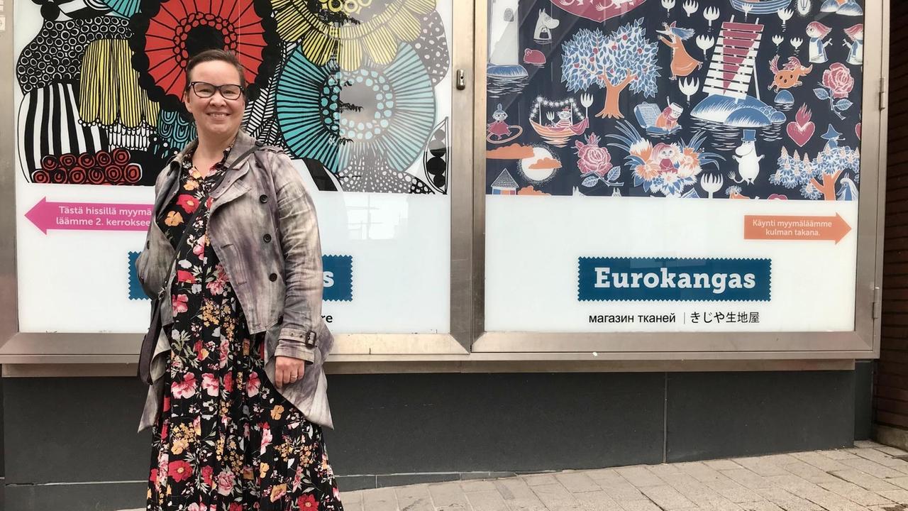 Eine Frau in buntem Kleid und Jacke steht vor einer Werbeplakatwand. Eine Frau in buntem Kleid und Jacke steht vor einer Werbeplakatwand.