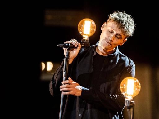 Tim Bendzko steht auf einer Bühne, die mit großen Glühlampen dekoriert ist.