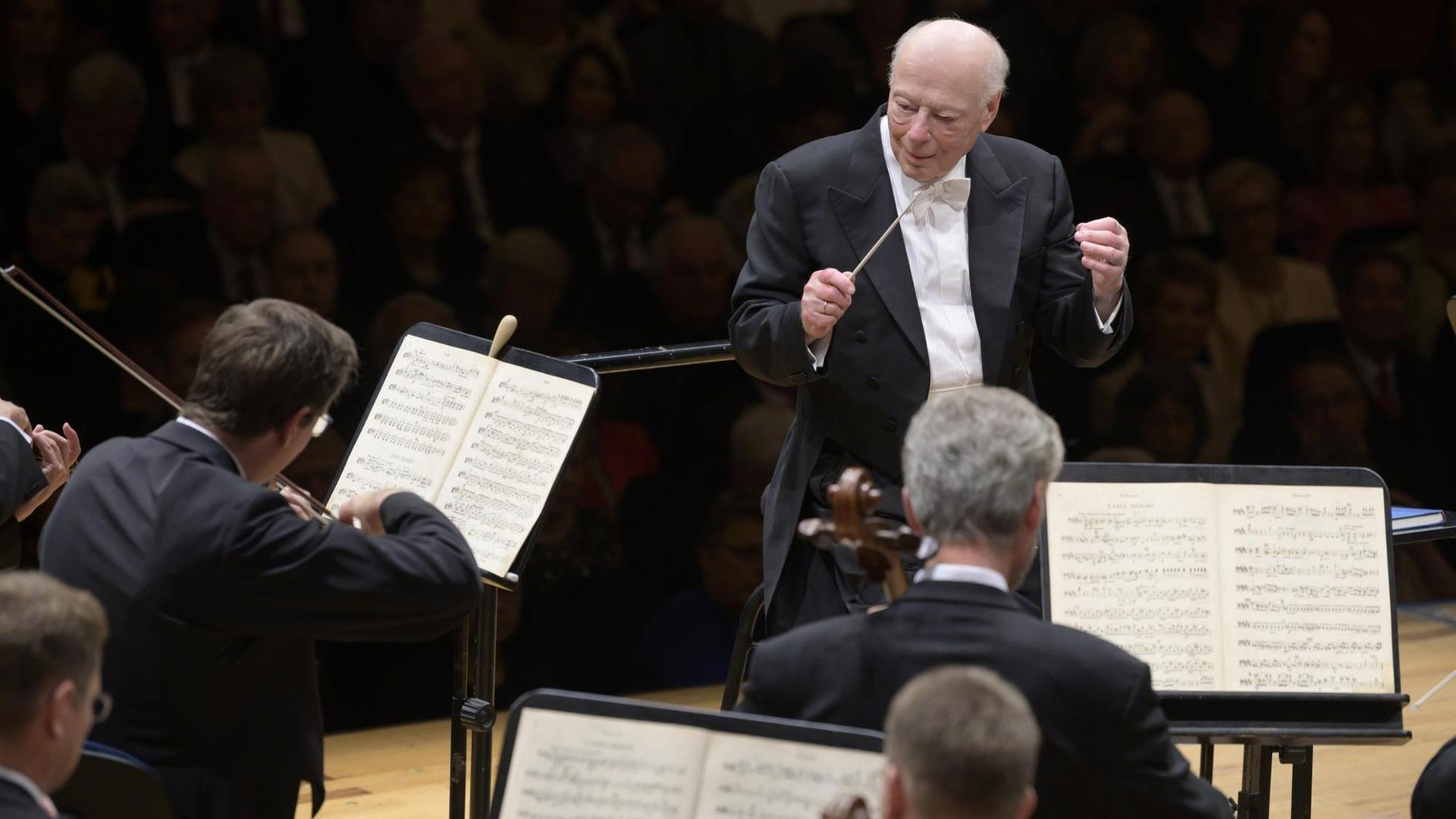 Bernard Haitink auf der Bühne vor dem Orchester. Zu sehen ist der Dirigent mit Taktstock in der Hand, er blickt nach links, vor ihm sitzen Streicher.