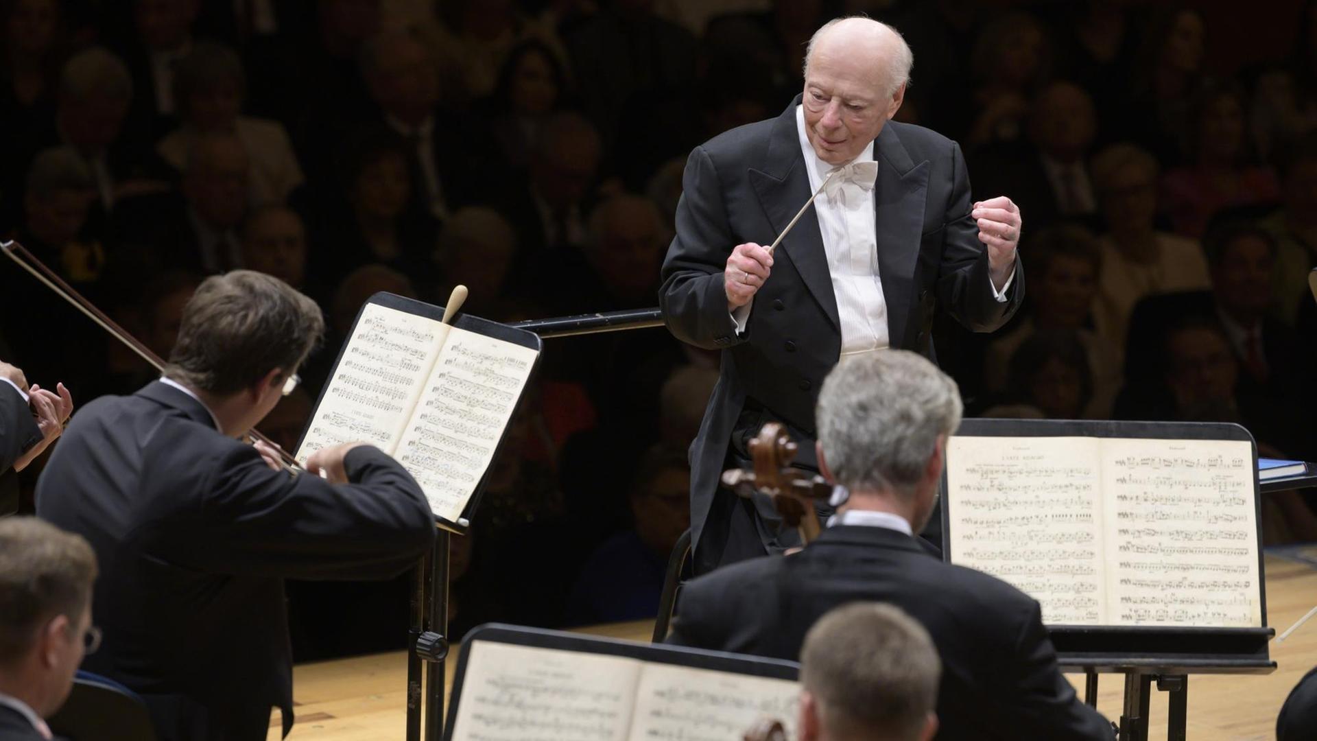 Bernard Haitink auf der Bühne vor dem Orchester. Zu sehen ist der Dirigent mit Taktstock in der Hand, er blickt nach links, vor ihm sitzen Streicher. Bernard Haitink auf der Bühne vor dem Orchester. Zu sehen ist der Dirigent mit Taktstock in der Hand, er blickt nach links, vor ihm sitzen Streicher.