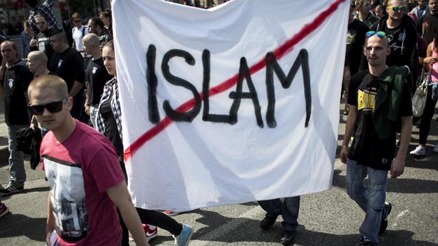 Demonstranten tragen ein weißes Stofftuch mit der rot durchgestrichenen Aufschrift "Islam".