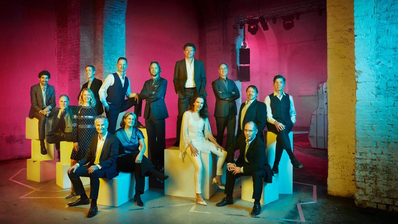 Die Musiker des Ensembles stehen und sitzen in einer bunt beleuchteten Ecke eines Betonbaus mit unterschiedlichen Sitzquadern. Die Musiker des Ensembles stehen und sitzen in einer bunt beleuchteten Ecke eines Betonbaus mit unterschiedlichen Sitzquadern.
