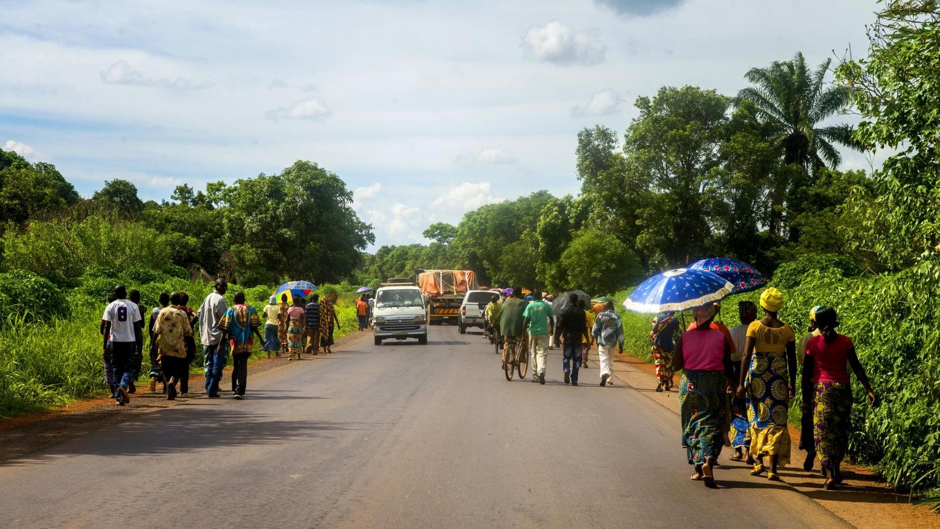 An den Seiten einer Straße im Kongo wandern Menschen entlang, um an ihr Ziel zu kommen. An den Seiten einer Straße im Kongo wandern Menschen entlang, um an ihr Ziel zu kommen.