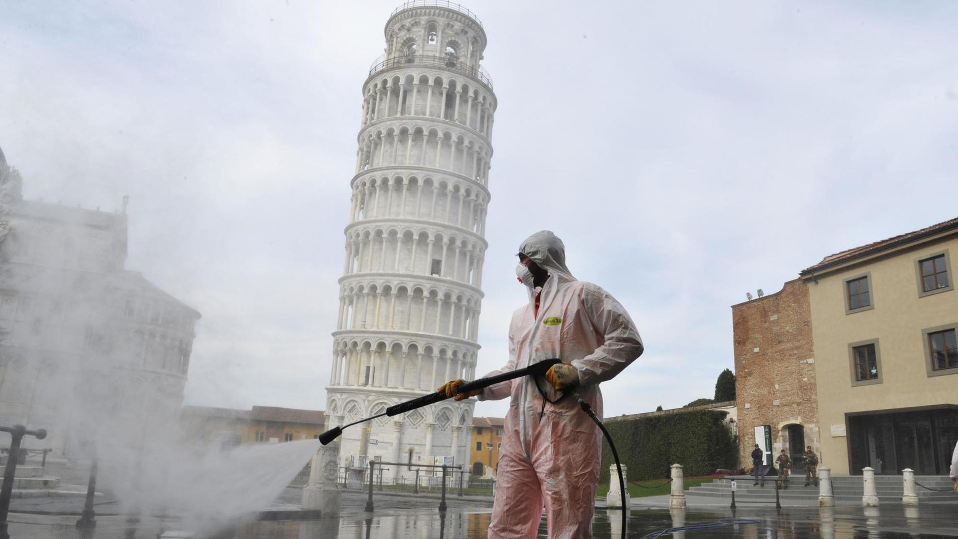 Ein Arbeiter in kompletter Schutzkleidung führt am 17. März 2020 in Pisa auf der Piazza dei Miracoli sanitäre Maßnahmen für den Coronavirus-Notfall durch. Im Hintergrund ist der bekannte schiefe Turm von Pisa zu sehen. Ein Arbeiter in kompletter Schutzkleidung führt am 17. März 2020 in Pisa auf der Piazza dei Miracoli sanitäre Maßnahmen für den Coronavirus-Notfall durch. Im Hintergrund ist der bekannte schiefe Turm von Pisa zu sehen.