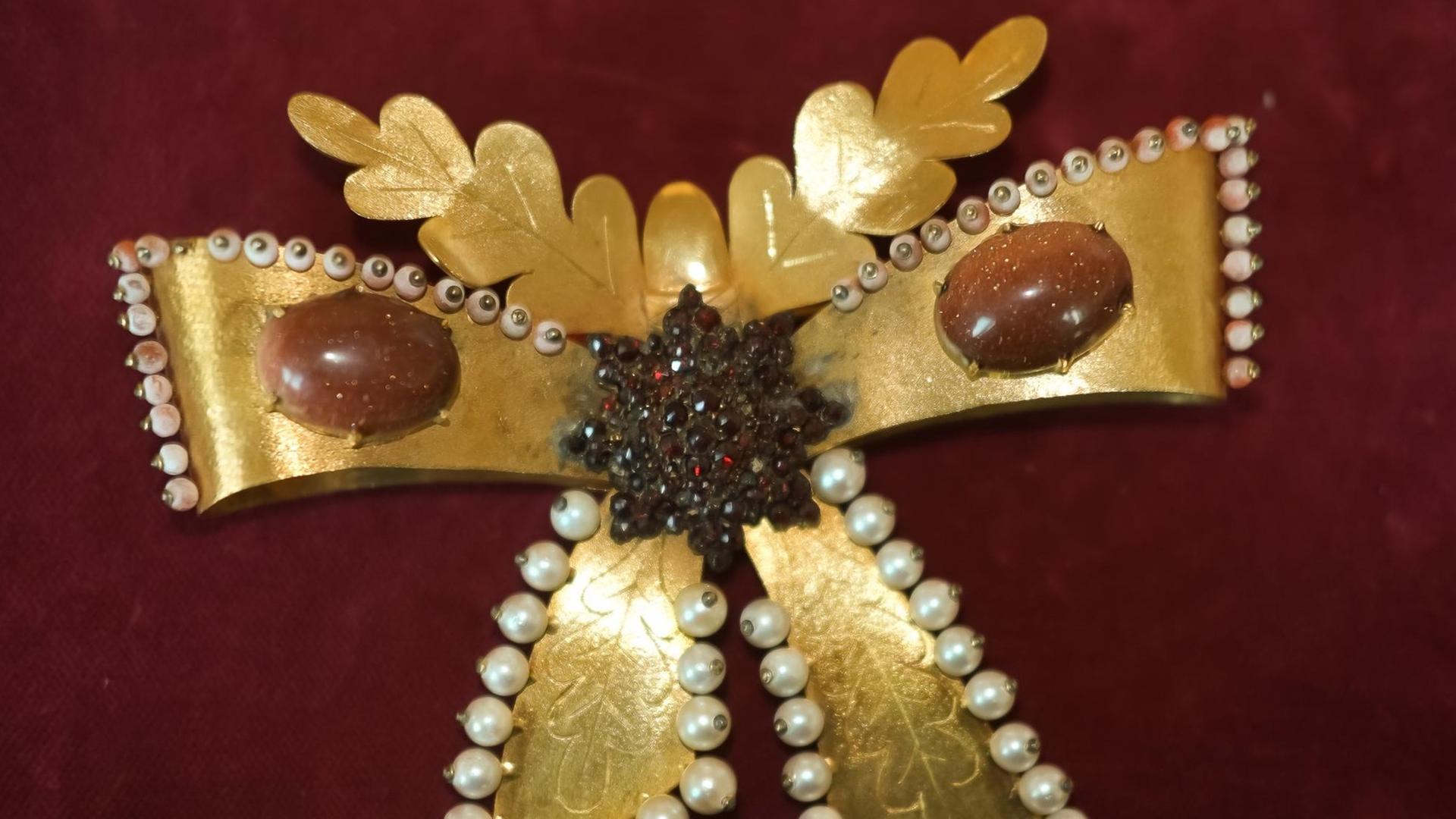 eine goldene Haarspange in Schmetterlingsform, an den Rändern besetzt mit kleinen weißen Perlen, links und rechts ovale rote Steine eine goldene Haarspange in Schmetterlingsform, an den Rändern besetzt mit kleinen weißen Perlen, links und rechts ovale rote Steine