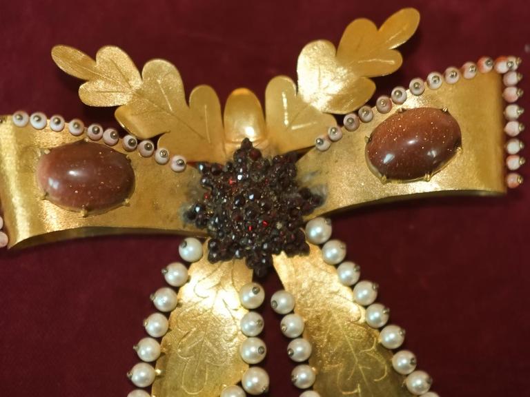eine goldene Haarspange in Schmetterlingsform, an den Rändern besetzt mit kleinen weißen Perlen, links und rechts ovale rote Steine