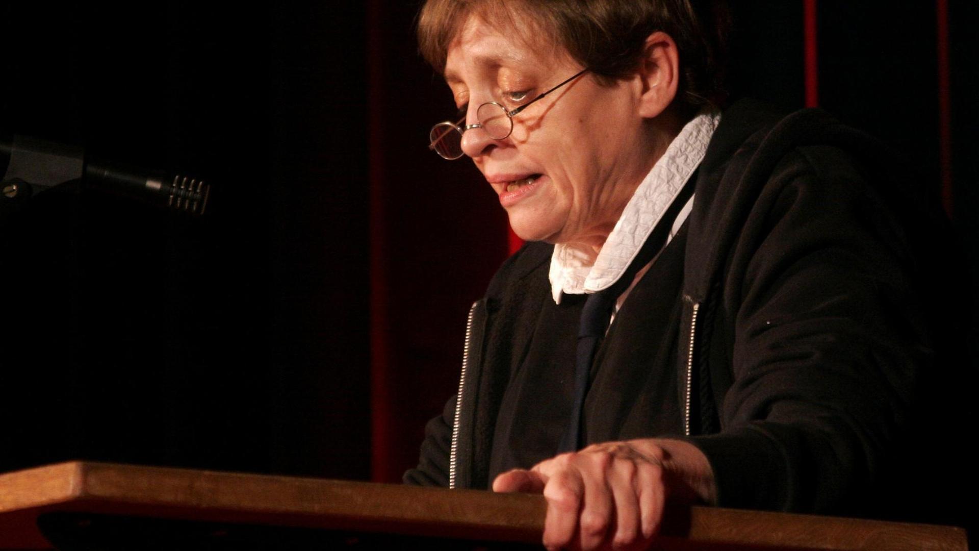 Katharina Thalbach sitzt an einem Holztisch und liest. Katharina Thalbach sitzt an einem Holztisch und liest.