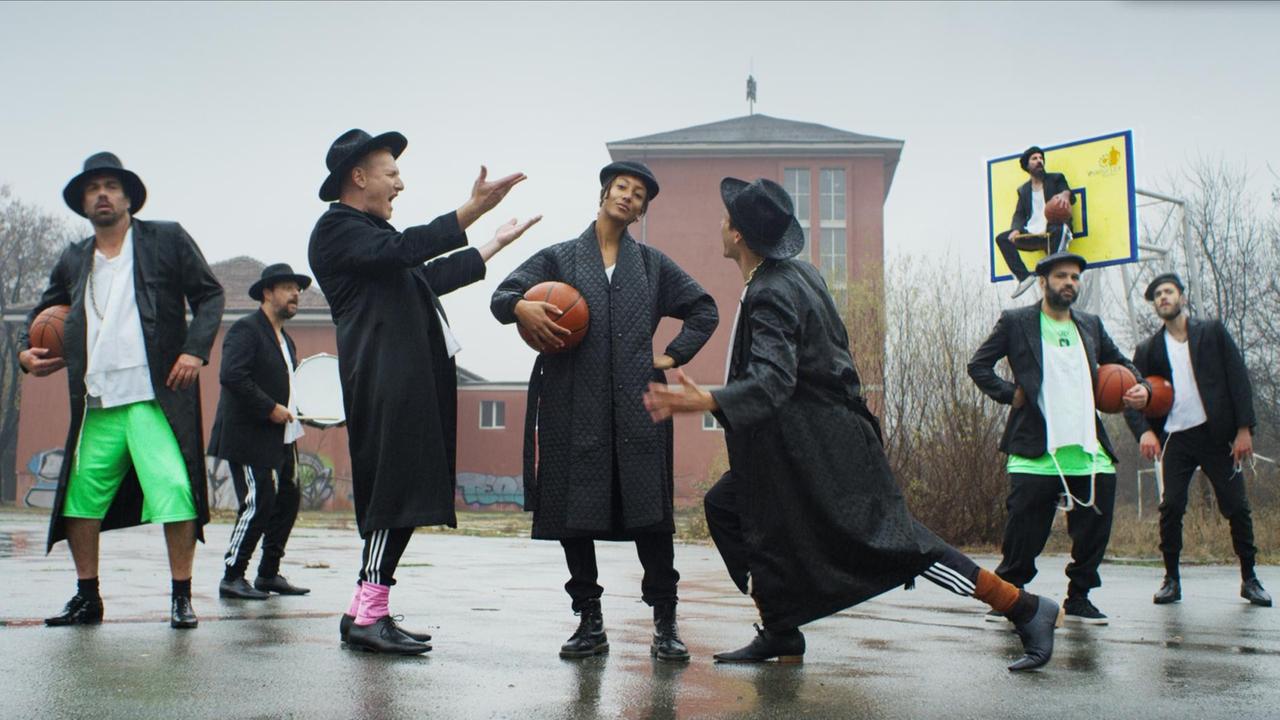 Die Bandmitglieder inszenieren sich auf einem Basketballplatz. Alle tragen einen Hut, einige einen Basketball unter dem Arm. Die Bandmitglieder inszenieren sich auf einem Basketballplatz. Alle tragen einen Hut, einige einen Basketball unter dem Arm.