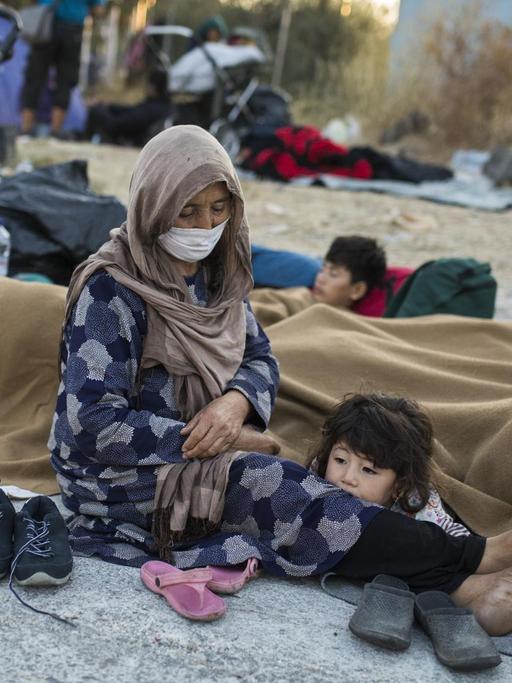Eine Frau mit ihren Kindern sitzt am Rande einer Straße in der Nähe des ausgebrannten Flüchtlingslagers Moria.