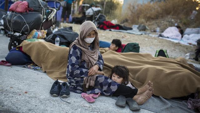 Eine Frau mit ihren Kindern sitzt am Rande einer Straße in der Nähe des ausgebrannten Flüchtlingslagers Moria.