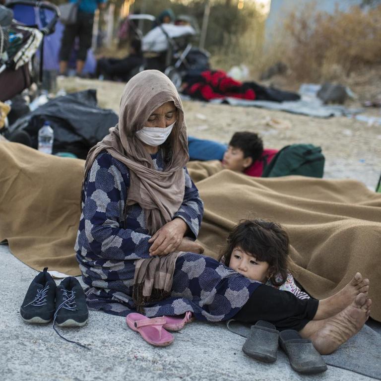 Eine Frau mit ihren Kindern sitzt am Rande einer Straße in der Nähe des ausgebrannten Flüchtlingslagers Moria.