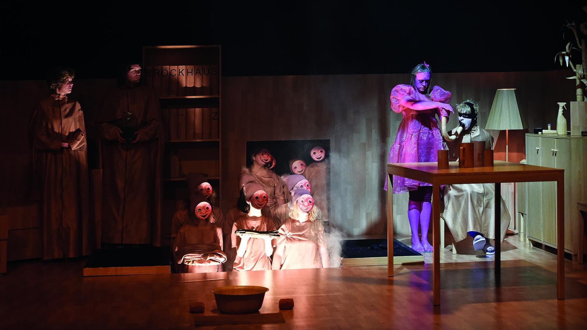 Eine Szene aus dem Theaterstück "Das Deutschland". Neben den vier Hauptdarstellern, sind zehn Personen mit roten, lachenden Masken, in Umhängen und langen Zipfelmützen zu sehen. Eine Szene aus dem Theaterstück "Das Deutschland". Neben den vier Hauptdarstellern, sind zehn Personen mit roten, lachenden Masken, in Umhängen und langen Zipfelmützen zu sehen.