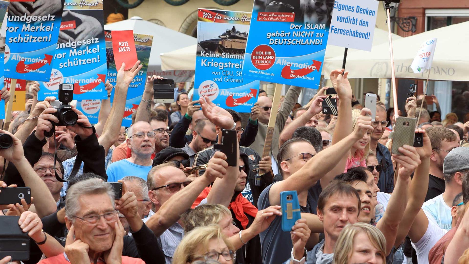 Demonstranten halten am 26.08.2017 am Rande einer ahlkampfveranstaltung der CDU mit Bundeskanzlerin Merkel auf dem Marktplatz in Quedlinburg (Sachsen-Anhalt) Plakate der Partei Alternative für Deutschland (AfD).