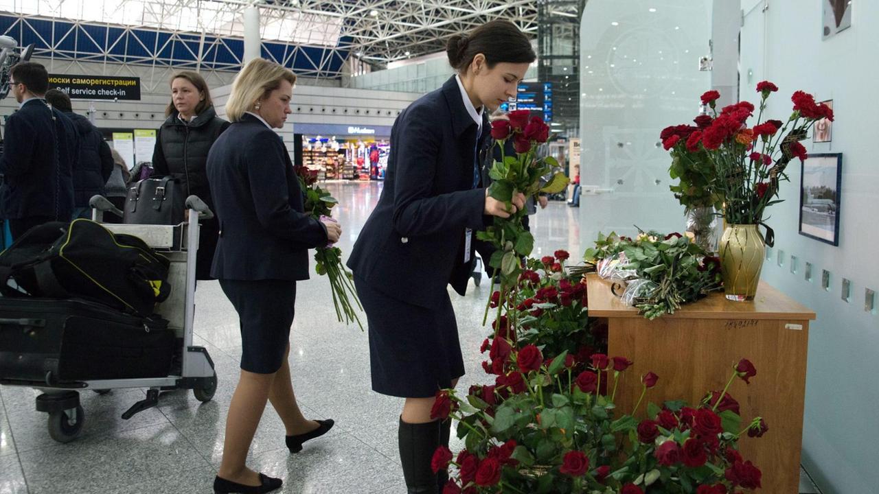Eine Frau in dunkler Uniform beugt sich nach vorn und legt am Flughafen von Sotschi eine Blume in Gedenken an die Absturz-Opfer nieder.