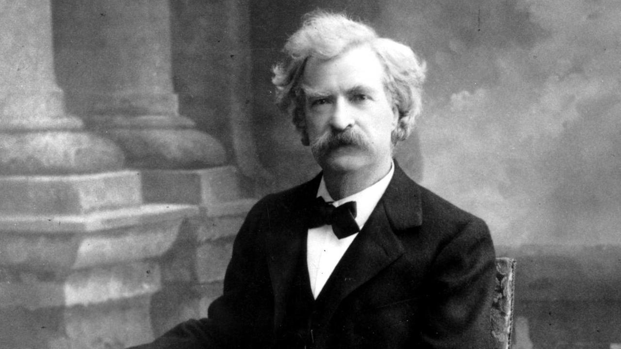 Mark Twain sitzt in einem dunklen Anzug auf einem Stuhl. Mark Twain sitzt in einem dunklen Anzug auf einem Stuhl.