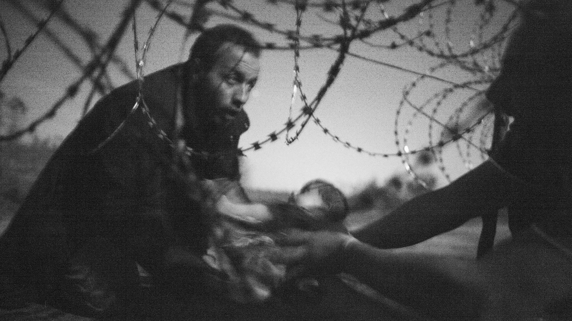 Flüchtlinge reichen ein Baby durch den Stacheldrahtzaun an der serbisch-ungarischen Grenze. Flüchtlinge reichen ein Baby durch den Stacheldrahtzaun an der serbisch-ungarischen Grenze.