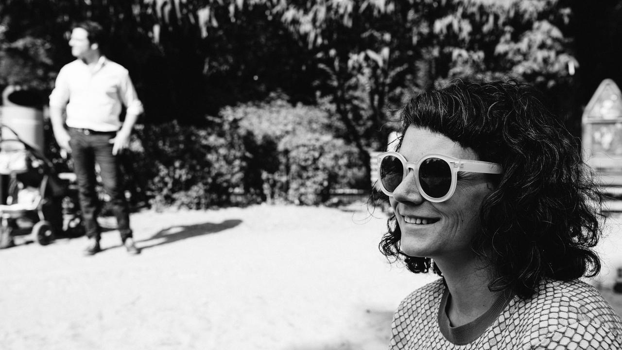 Schwarz-Weiß-Porträtaufnahme von Gili Waldman mit großer Sonnenbrille bei einem letzten Spaziergang in Berlin. Im Hintergrund unscharf Ofer Waldman. Schwarz-Weiß-Porträtaufnahme von Gili Waldman mit großer Sonnenbrille bei einem letzten Spaziergang in Berlin. Im Hintergrund unscharf Ofer Waldman.
