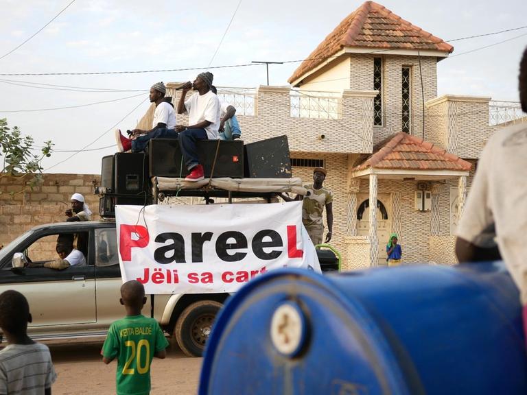 Die Rapper der senegalesischen Protestbewegung "Y’en a Marre" – "Wir haben es satt". Sie sitzen auf einem Auto und fahren durch eine staubige Straße.