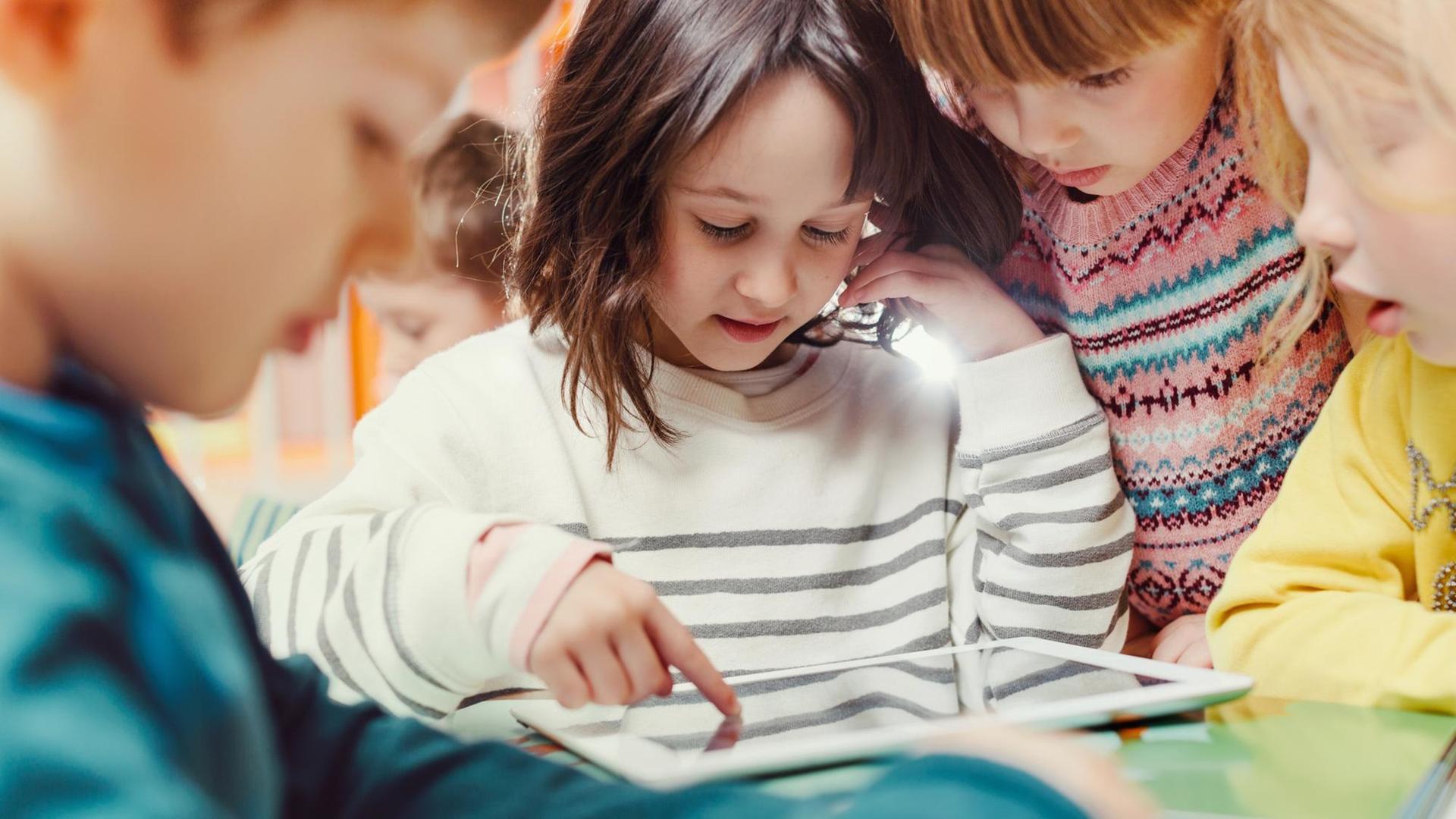 Mehrere Kinder schauen gemeinsam auf das Display eines Tablets. Mehrere Kinder schauen gemeinsam auf das Display eines Tablets.