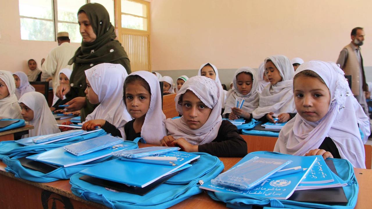 Mädchen mit weißem Kopftuch sitzen in Schulbänken. Vor ihnen auf den Tischen liegen Taschen in Unicef-blau. Mädchen mit weißem Kopftuch sitzen in Schulbänken. Vor ihnen auf den Tischen liegen Taschen in Unicef-blau.