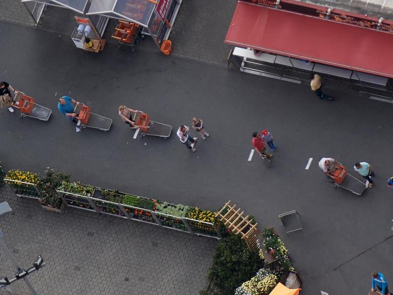 Kunden eines Baumarktes stehen vor dem Eingang mit Abstand in einer Schlange. Zur Eindämmung des Coronavirus hat NRW alle Ansammlungen ab drei Personen in der Öffentlichkeit verboten.