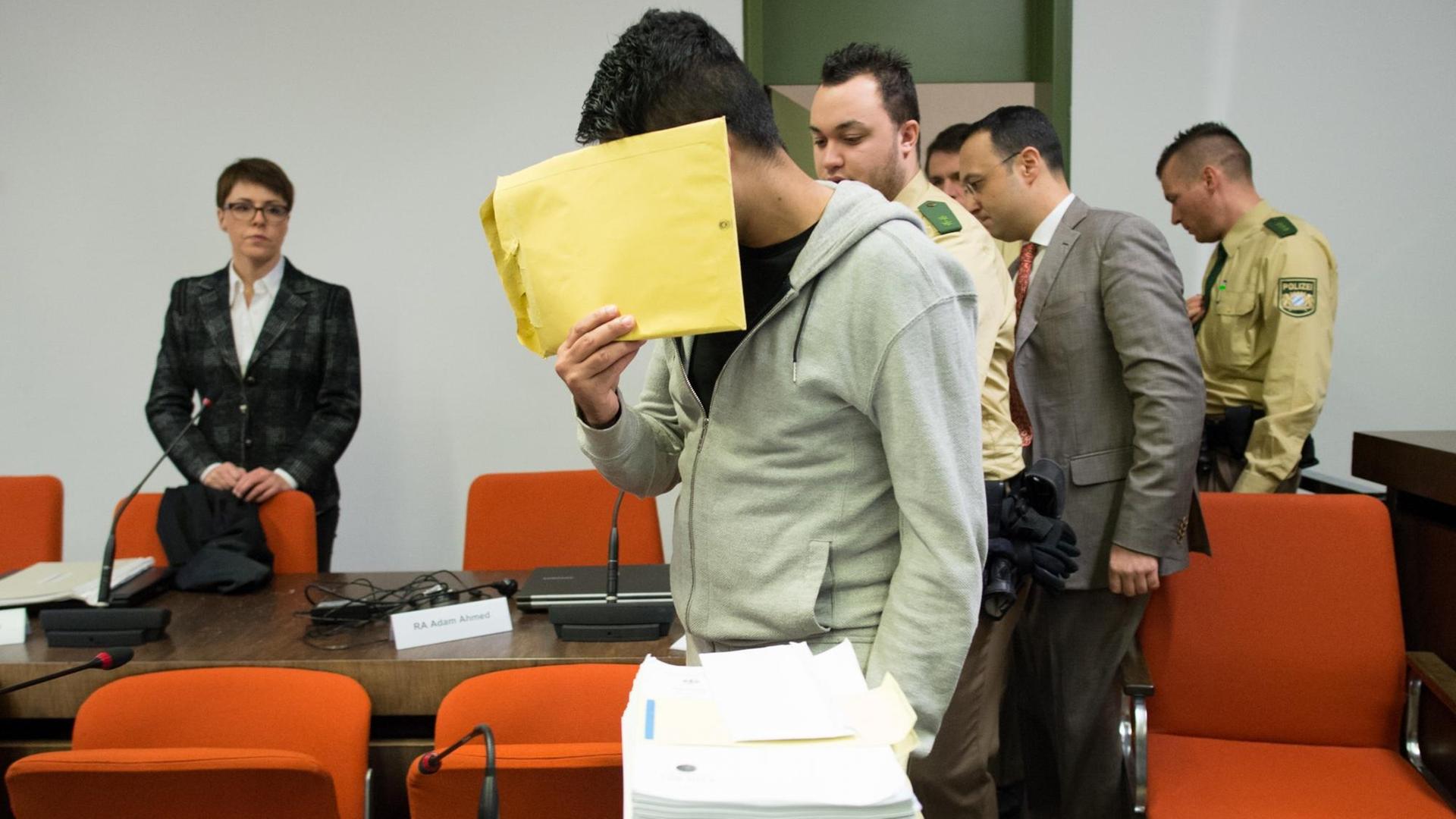 Ein junger Mann versteckt als Angeklagter am 20.01.2015 in einem Gerichtssaal sein Gesicht hinter einem Umschlag. Um ihn herum stehen Polizisten und weitere Personen. Ein junger Mann versteckt als Angeklagter am 20.01.2015 in einem Gerichtssaal sein Gesicht hinter einem Umschlag. Um ihn herum stehen Polizisten und weitere Personen.