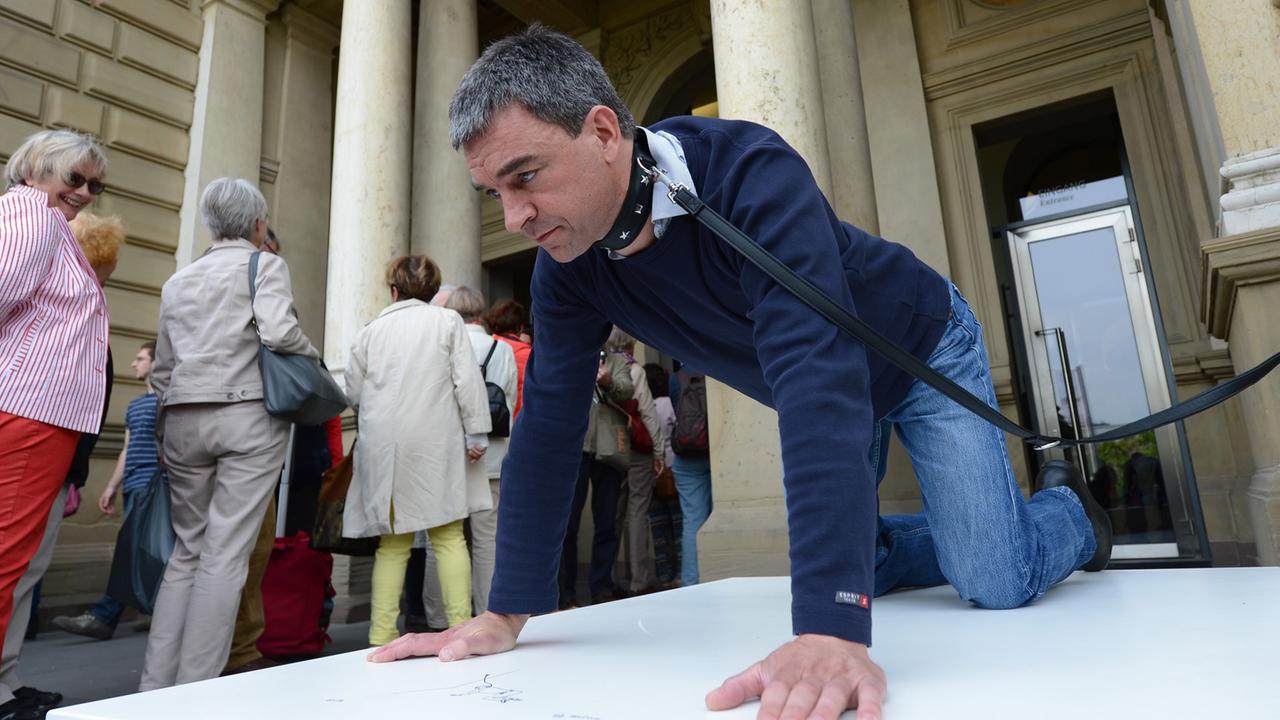 Ein Statist ist am 06.05.2014 am Eingang des Städel-Museums in Frankfurt am Main (Hessen) bei der Vorführung von Erwin Wurms "einmal Hund sein" mit einem Hundehalsband angeleint. Ein Statist ist am 06.05.2014 am Eingang des Städel-Museums in Frankfurt am Main (Hessen) bei der Vorführung von Erwin Wurms "einmal Hund sein" mit einem Hundehalsband angeleint.