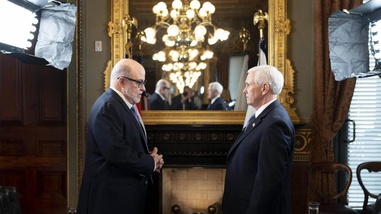 Zwei Männer (Ex-US-Vizepräsident Mike Pence und Journalist Mark Levin) stehen sich in einem herrschaftlichen Raum gegenüber. Im Hintergrund hängt ein Spiegel, in dem sich ein Kronleuchter spiegelt. Zwei Männer (Ex-US-Vizepräsident Mike Pence und Journalist Mark Levin) stehen sich in einem herrschaftlichen Raum gegenüber. Im Hintergrund hängt ein Spiegel, in dem sich ein Kronleuchter spiegelt.