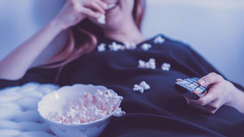 Eine Frau liegt auf einer Couch und ißt Popcorn.