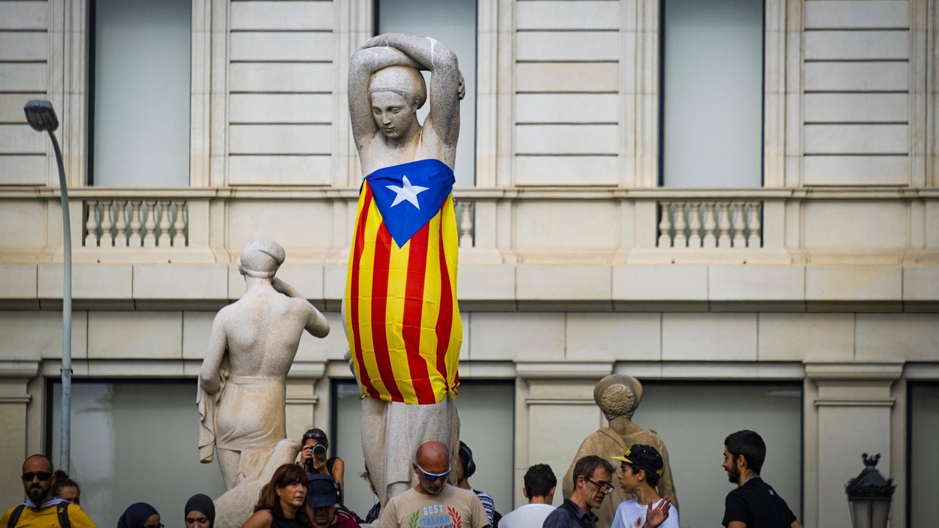 Demonstranten haben eine Frauenstatue auf der Plaxa Catalunya in Barcelona in eine katalonische Flagge eingewickelt.