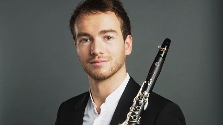 Joë Christophe mit kurzen braunen Haaren und Dreitagebart lächelt in die Kamera, während sein Instrument an der Schulter lehnt.