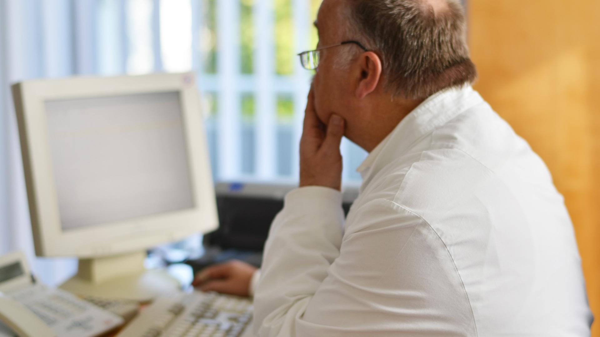 Ein Hausarzt sitzt in seinem Beratungszimmer vor einem Computer Ein Hausarzt sitzt in seinem Beratungszimmer vor einem Computer