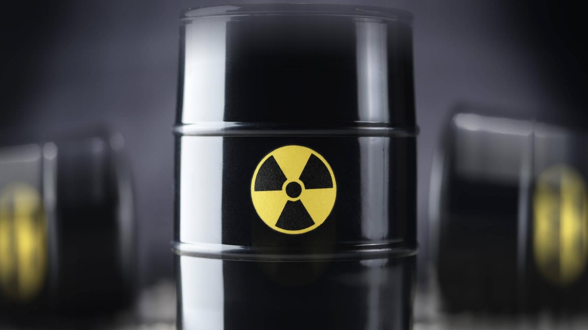 Drei schwarze Atommüll-Fässer, wobei eines im Vordergrund in der Mitte scharf abgebildet ist, im Hintergrund zwei weitere Fässer unscharf. Drei schwarze Atommüll-Fässer, wobei eines im Vordergrund in der Mitte scharf abgebildet ist, im Hintergrund zwei weitere Fässer unscharf.