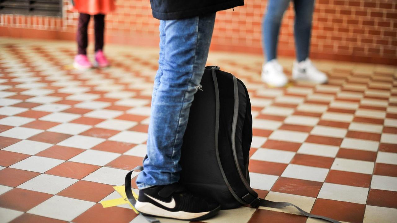 Schülerbeine in Jeans und Turnschuhen stehen mit Abstand voneinander im Flur einer Schule. Schülerbeine in Jeans und Turnschuhen stehen mit Abstand voneinander im Flur einer Schule.