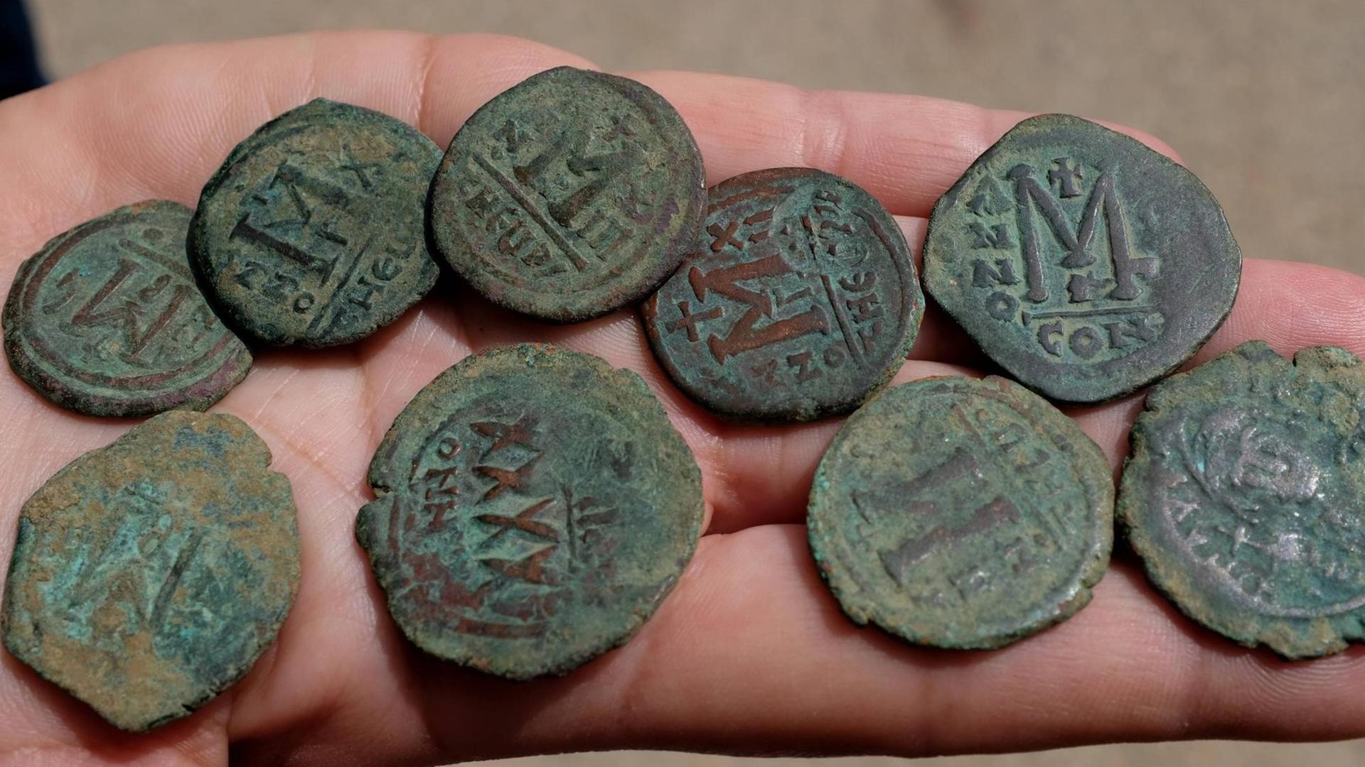 Neun antike Münzen liegen auf einer Handfläche.